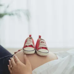 A creative and symbolic close-up of tiny red sneakers resting on the baby bump, announcing the little one's arrival in a fun, modern way.