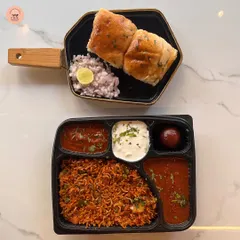 A taste of Mumbai in a box. This meal features spicy tawa pulao with a side of pav bhaji, raita, and a gulab jamun, accompanied by buttered pavs. It's a favorite for casual gatherings and parties.