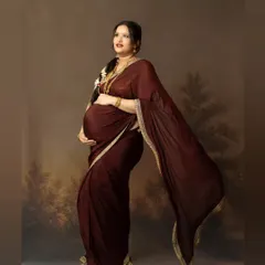 A graceful full-length portrait of a woman in a traditional maroon saree, captured against a painted landscape backdrop. We aim to create images that feel like classic paintings, celebrating cultural heritage.
