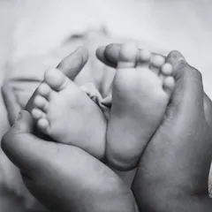 A black and white detail shot of a parent's hands gently holding their newborn's feet, a powerful and artistic image.