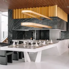 For the Tellado Villas, the goal was to create a confluence of social spaces. This open-plan dining and kitchen area uses bold forms, like the sculptural dining island and dramatic black marble, contrasted with the warmth of a wooden ceiling. It is a space designed for gathering, conversation, and shared experiences.