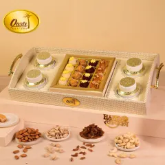 A luxurious white wicker tray hamper, designed for sharing. It features a central box of assorted sweets, surrounded by jars of premium dry fruits, making it a wonderful centerpiece for any celebration.