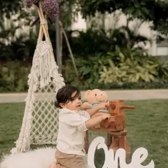 Celebrating a first birthday outdoors with a teepee, teddy bear, and wooden props for a rustic, natural feel.