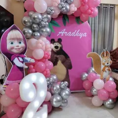 A classic Masha and the Bear theme for Aradhya's second birthday. The setup includes large character cutouts, a light-up number two, and a pink and silver balloon garland to complete the look.