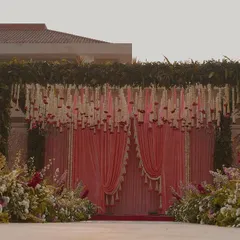 The front view of our floral mandap, showcasing the intricate details. A canopy of dense greenery is adorned with hanging strings of tuberose and roses, set against soft pink drapes for a romantic touch.