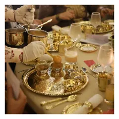 We honour India's rich culinary legacy with our traditional silver service. This image showcases an elaborate sit down feast, where guests are served from magnificent hammered brass and silver thalis, reflecting a timeless elegance and a truly royal dining experience.