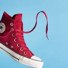 A vibrant, dynamic shot of a red high-top sneaker suspended against a solid blue background. This style of creative product photography grabs attention and is ideal for social media and ad campaigns.