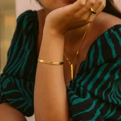 A woman wearing a gold engraved cuff bracelet. This shot shows how the bracelet can be a standalone statement piece, adding a touch of personalized elegance to her outfit.