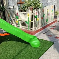 A view of our safe and inviting outdoor play area, complete with a slide and soft turf. This space is perfect for developing gross motor skills and enjoying the fresh air.