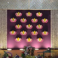 A unique Ganpati backdrop featuring a deep purple wall adorned with lotus flower motifs made from petals. The design is framed by hanging pearl strings, creating a royal and elegant look.