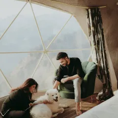 A cozy indoor moment with a couple and their fluffy Samoyed dog in a beautiful geodesic dome in the mountains.