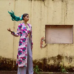 A full-length shot showing the entire co-ord set with the long jacket. The combination of floral and stripes, along with the pop of color in the hair, makes for an unforgettable festive outfit.