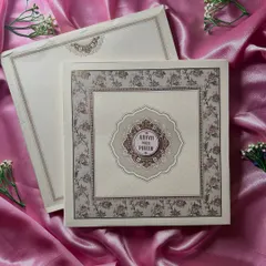 This elegant invitation suite features a soft, pastel color palette with a beautiful floral border. The central medallion with the couple's names adds a touch of classic charm, presented on a bed of pink satin to highlight its luxury.