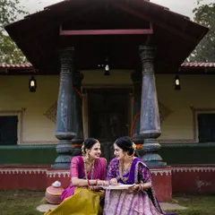 A wider shot from the same festive shoot, showing the women in front of a traditional house, capturing the full cultural context.