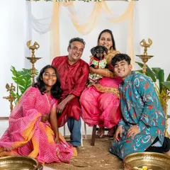 A happy family portrait from a Diwali mini-session. The whole family, dressed in colorful traditional outfits, smiles brightly with their adorable dachshund.