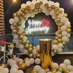 An elegant and classic anniversary decoration with a full circular arch of gold and white balloons. The "Happy Anniversary" neon sign with a heart detail adds a romantic touch, perfect for an intimate party.