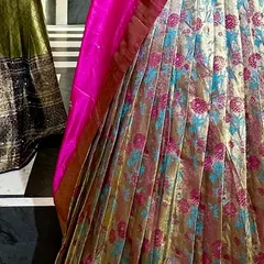 A close-up of the fabric and pleats of the floral brocade saree lehenga. The combination of gold, pink, and blue creates a rich and festive look.