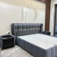 This elegant grey velvet bed features a tufted, winged headboard and a matching upholstered frame. It is paired with a unique fluted bedside table with a black glass top, combining classic comfort with modern details.