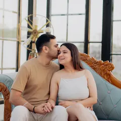 A sweet forehead kiss captured during an indoor session. The elegant glasshouse setting with vintage furniture provides a sophisticated and romantic atmosphere.