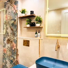 A detail shot of the bathroom with floral tiles, showcasing the wall-mounted toilet and gold-finished flush plate. The floating shelves provide a stylish spot for plants and toiletries.