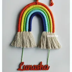 A bright and cheerful macrame rainbow with the name 'Lunasha' hanging below. This piece brings so much color and joy to a room. You can pick any colors you like, from vibrant rainbow shades to more muted, earthy tones, to create the perfect wall hanging for your child.