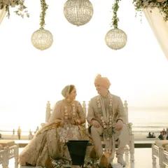 A beautiful moment between the bride and groom as they sit at the mandap, sharing a look of love with the ocean behind them. The hanging chandeliers add a touch of elegance.