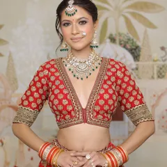 A full portrait of a stunning bride in her red lehenga. The makeup is designed to enhance her features, with a focus on glowing skin and expressive eyes, making her look and feel like royalty.