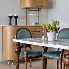 This dining area features a sophisticated bar cabinet, perfect for entertaining. The classic wooden chairs with teal velvet upholstery add a touch of vintage glamour, while the modern bar unit provides practical storage.