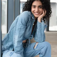 A smiling shot of a model with natural curls in a denim outfit. The makeup is subtle, designed to look like her own skin but better, perfect for a commercial or lifestyle photoshoot.