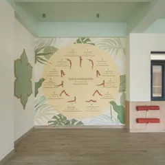 The serene yoga room, featuring a large "Surya Namaskara" mural that guides students through the sequence. The natural wood flooring and leafy graphics create a calm, grounded atmosphere for mindfulness and movement.