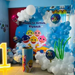 An underwater adventure with this Baby Shark theme for a first birthday. The setup includes a character-filled backdrop, an organic balloon arch creating a wave effect, and a light-up number '1'.