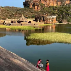 Two women in colorful sarees wash clothes by the river, with ancient temples and rocky hills in the background. This image beautifully blends the daily life of today with the history of the landscape.