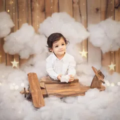 A quiet moment amidst the clouds for this one-year-old pilot. The setup includes a wooden plane, cotton clouds, and twinkling stars, creating a magical atmosphere for his first birthday portraits.