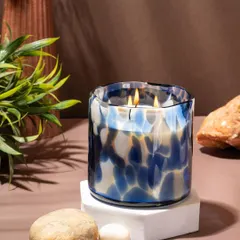 A styled lifestyle shot of a Lighthouse candle, using natural elements like stone and plants to create a serene, earthy mood. The focus is on showing how the home decor product fits into a calming personal space.