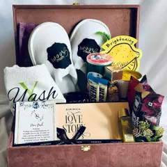 A full view of our personalized groom hamper in a luxurious dusty pink trunk. It features custom "Groom" slippers, a monogrammed towel, and a curated selection of self-care products and treats.