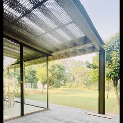 A detail of the steel and glass pavilion in Delhi. The roof is made of a perforated steel jaali, which casts dappled light onto the patio, mimicking the effect of a tree canopy.