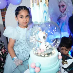 The birthday girl poses next to her incredible 'Frozen' snow globe cake. It's a moment of pure magic.