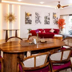 A complete view of a neo-classical living and dining area in a 4BHK at Sobha Royal Pavilion. The bold red sofa, solid wood dining table with cane chairs, and elegant wall mouldings create a space that is both grand and welcoming.