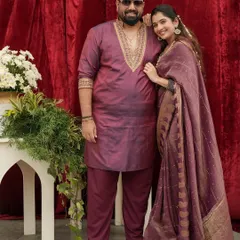 A full-length view of Tharun and Sonal's anniversary outfits. His kurta features intricate embroidery on the neckline, perfectly complementing her elegant saree.