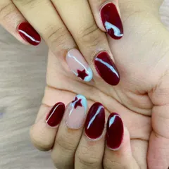 A patriotic-inspired look. This design combines a deep maroon polish with accent nails featuring a red star on a light blue and nude background.