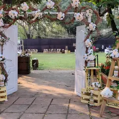 This rustic entrance features a freestanding white door, a welcome sign on an easel, and charming details like wooden crates and a ladder used as shelving for floral arrangements.
