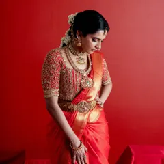 A moment of quiet contemplation, this image showcases the rich texture of the red silk saree and the intricate gold embroidery of the matching blouse. The traditional jewelry and floral hair adornment complete this quintessential bridal look.