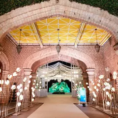 A whimsical pathway lined with glowing tulip-shaped lights leads guests through a brick archway into the main event space.