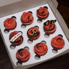 Celebrating new beginnings with this custom engagement cupcake box. The set features rich red velvet cupcakes with red and black frosting, accented with edible gold dust, and detailed fondant work like intertwined rings and custom initials.