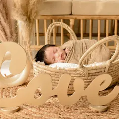 A newborn sleeps in a basket on a jute mat, with a large "LOVE" sign in the foreground. This setup combines rustic elements with a clear, heartfelt message.