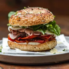 A fully loaded everything bagel sandwich. We stack it high with meats, cheeses, and fresh arugula for a satisfying and delicious meal.