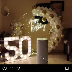 An elegant 50th birthday setup for an evening celebration. It features large marquee numbers, a simple balloon arch in white and gold, and a 'Happy Birthday' neon sign for a classy photo corner.