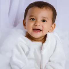 A classic sitter session portrait. This baby boy in a white robe gives a huge, happy smile, sitting in a cloud of white fluff.