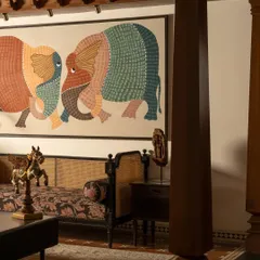 The living area, where a large Gond art piece becomes the focal point. The design balances the maximalist artwork with the classic elegance of the carved wooden furniture and Chettinad pillars.