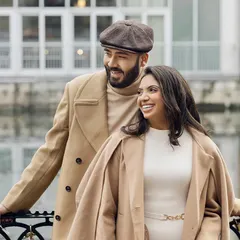 A candid moment of laughter by the water in London. The couple's outfits, featuring cozy coats and a classic newsboy cap, were chosen to reflect a relaxed yet polished aesthetic, perfect for a day spent together.